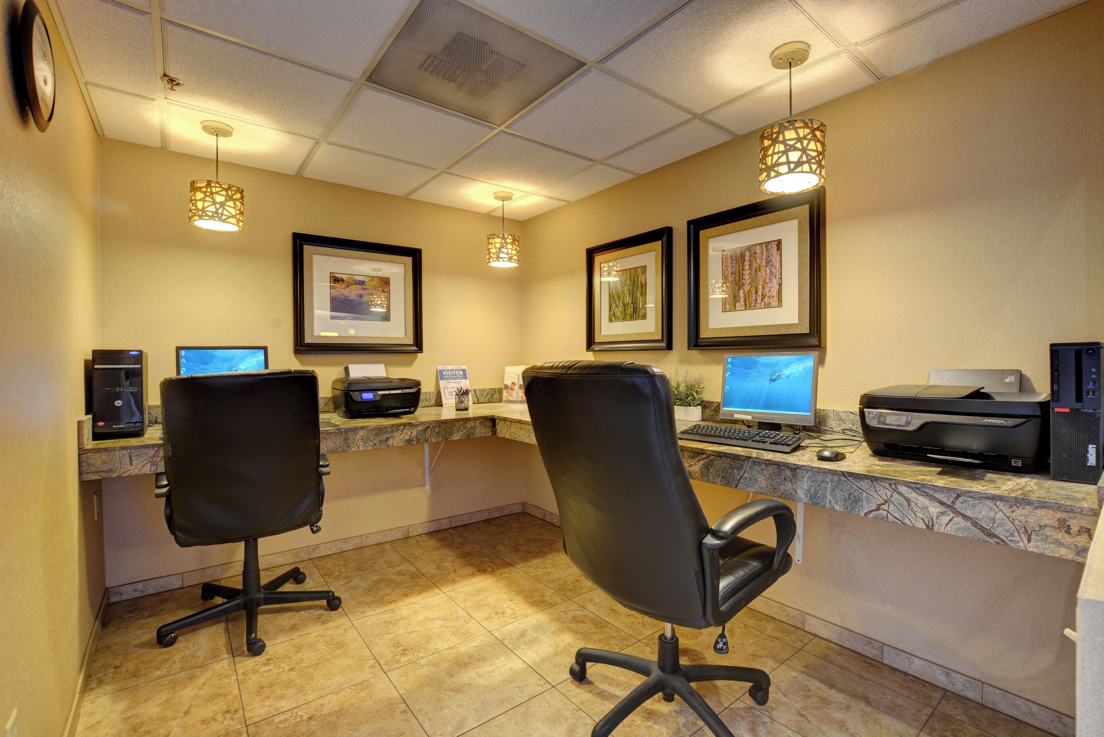 A reception area with two black office chairs, a marble counter, multiple computer monitors, framed artwork, and a printer.