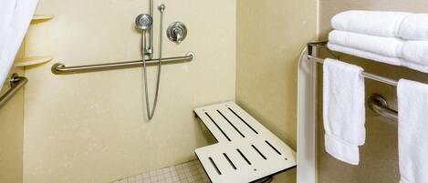 A small, accessible shower area with a grab bar, a white shower seat, and a towel rack with folded towels.