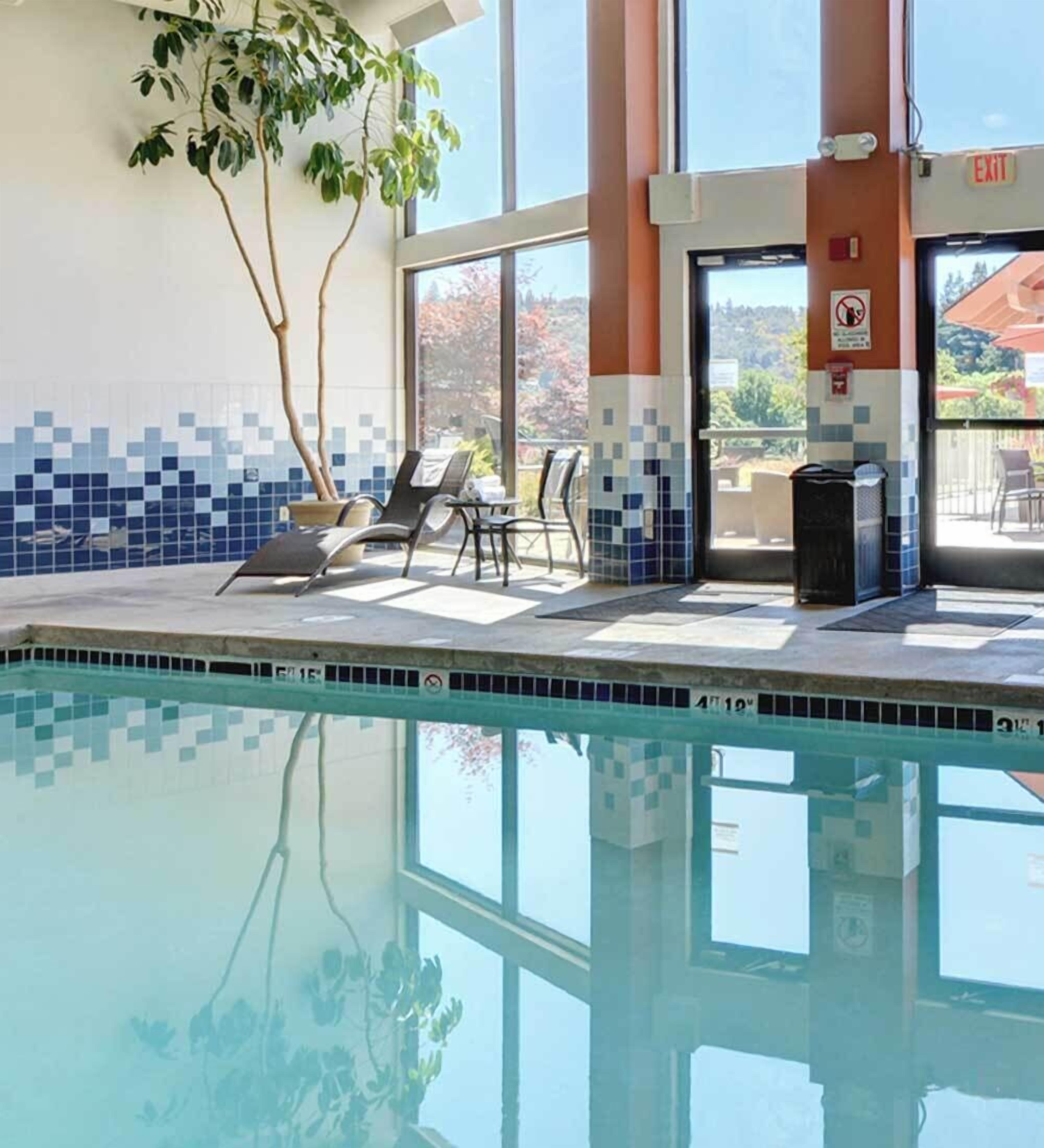 En indendørs swimmingpool med klart, blåt vand, omgivet af liggestole og en flisevæg med et blåt og hvidt mønster.