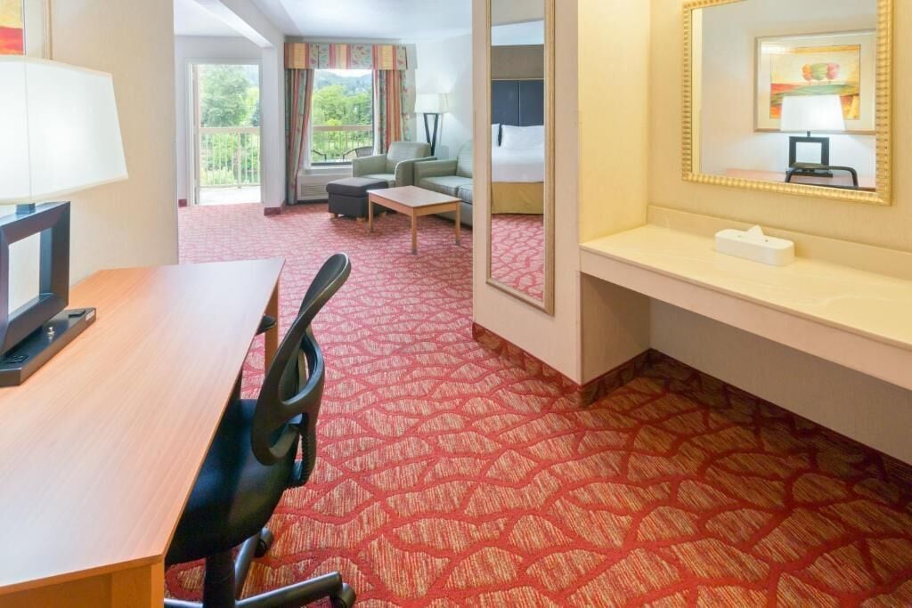Quarto de hotel com escrivaninha de madeira, cadeira de escritório preta, mesinha, sofá e uma cama.