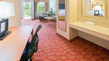Quarto de hotel com escrivaninha de madeira, cadeira de escritório preta, mesinha, sofá e uma cama.