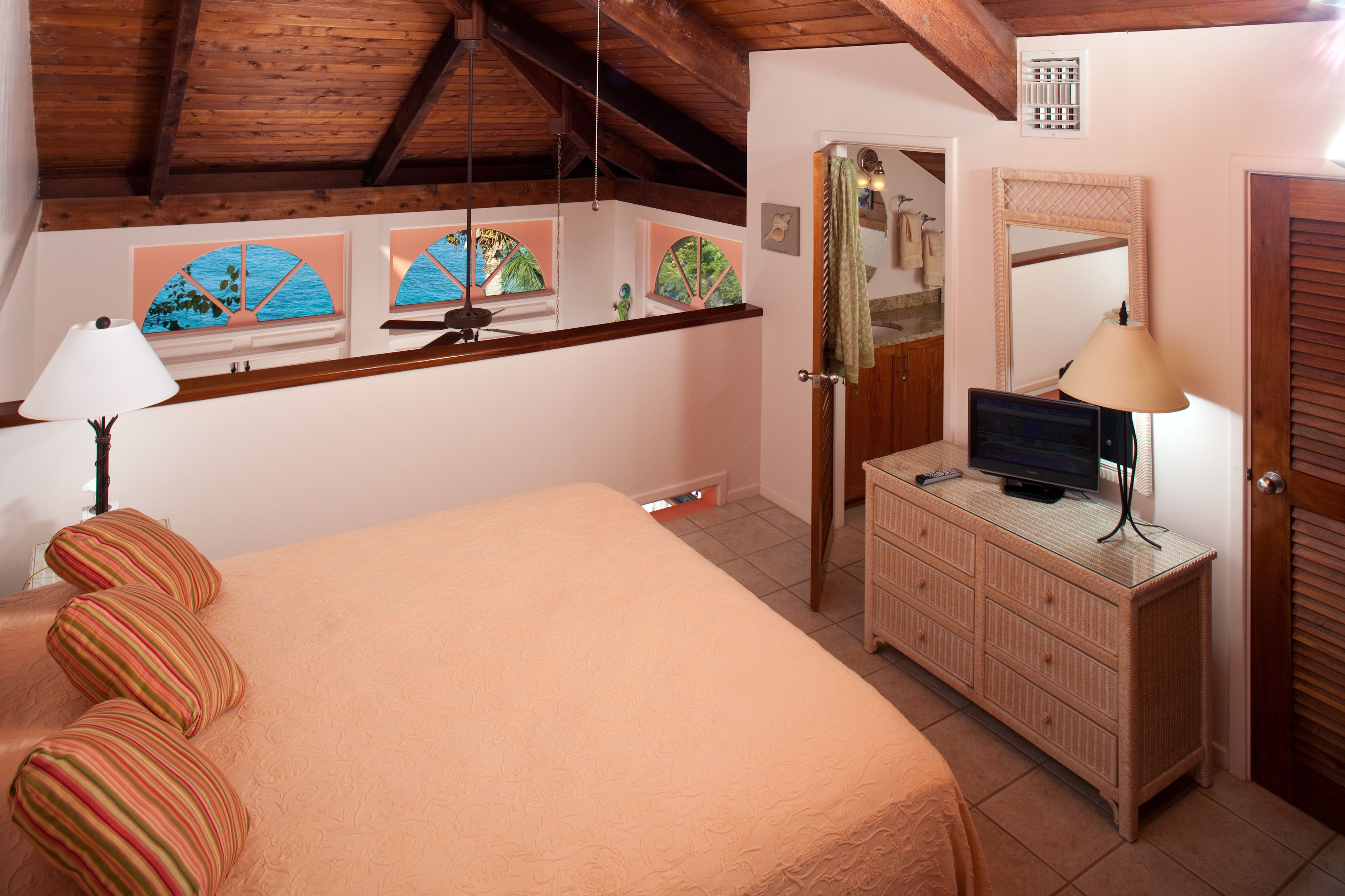 Un dormitorio con cama, cómoda, televisor y ventana con vista al mar.