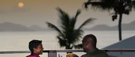 Two people sitting at a table outdoors with a view of the sea and mountains in the background.