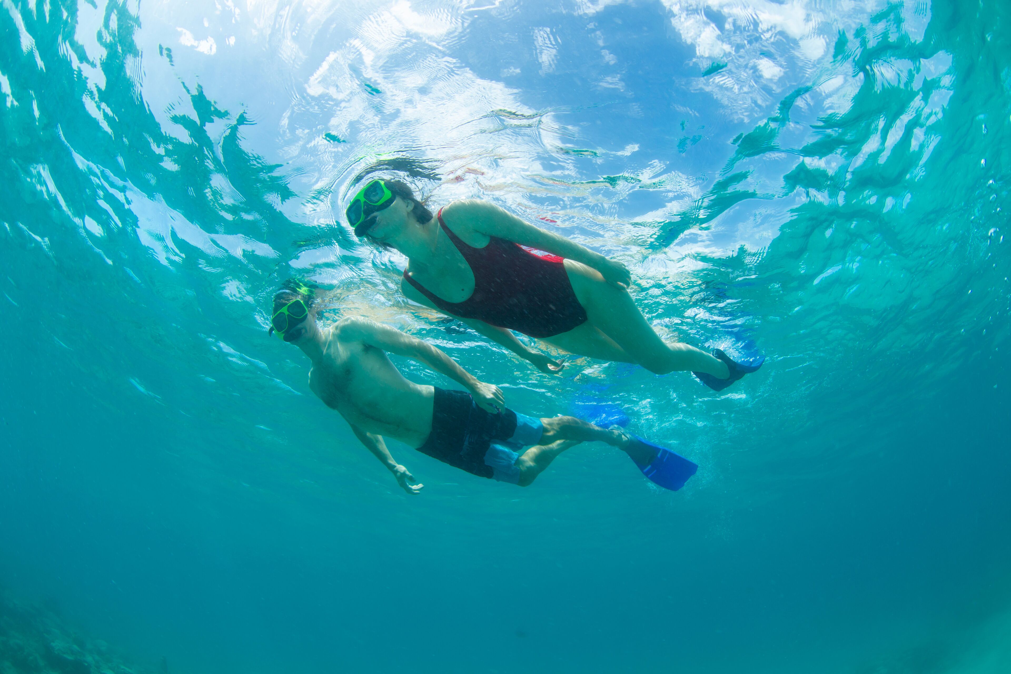 Zwei Personen schwimmen unter Wasser in einem klaren, blauen Pool.