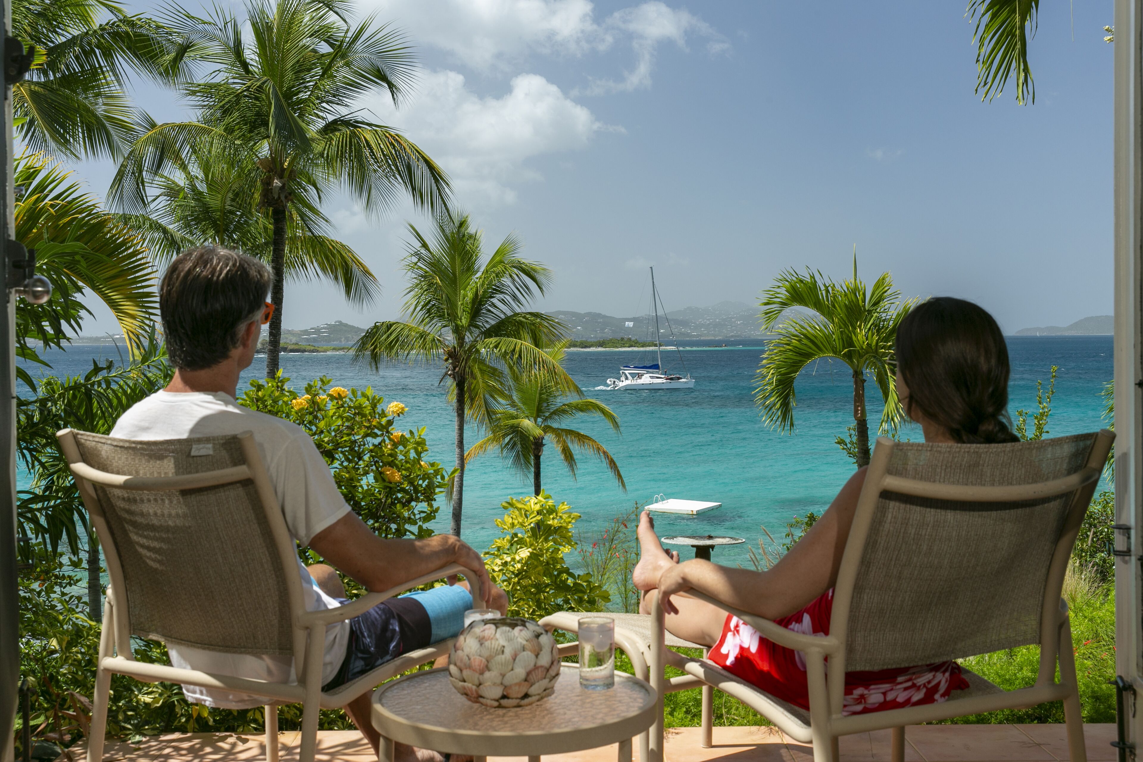 Two people seated at a table with a view of the ocean and a sailboat in the distance.