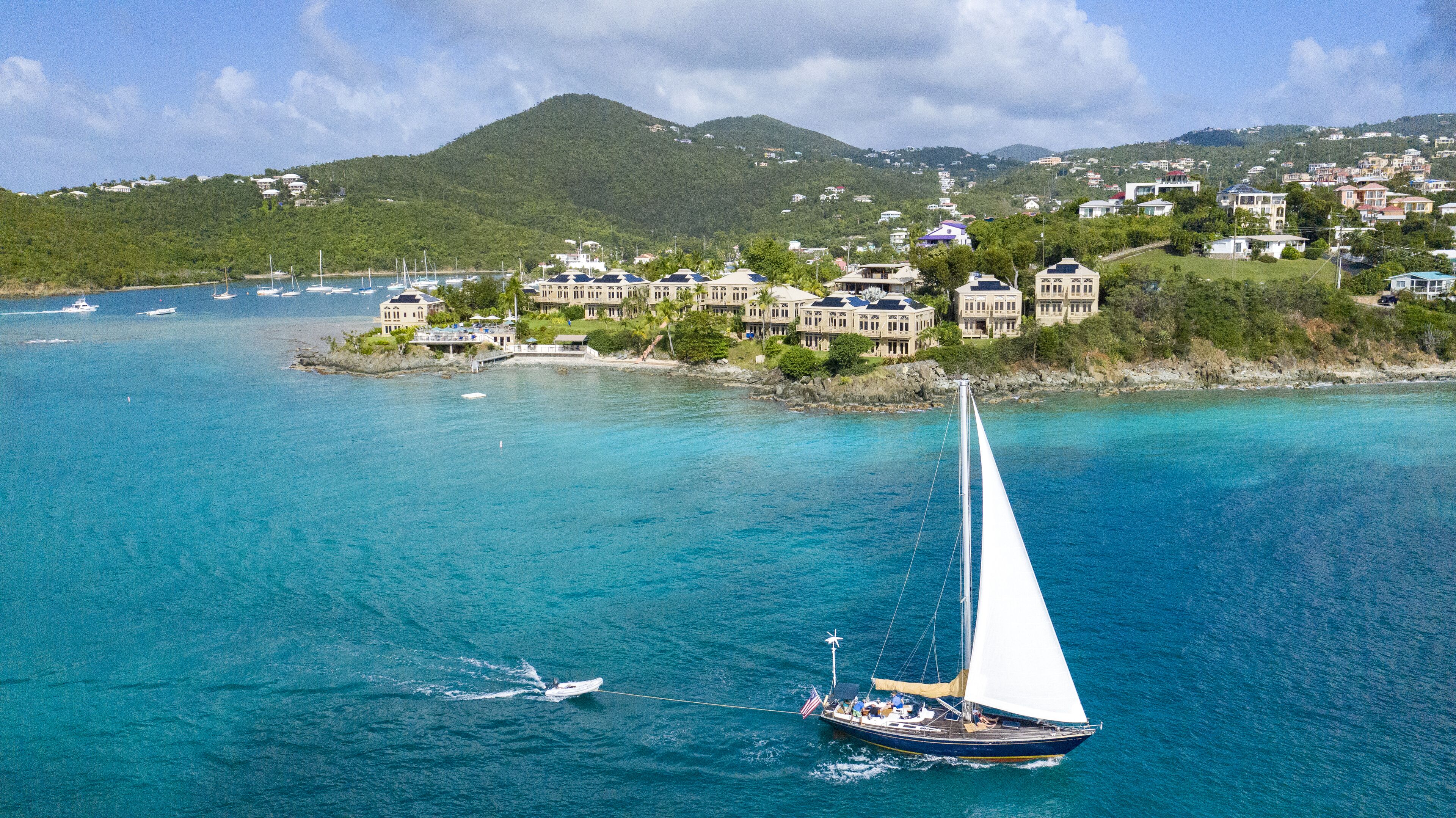 Un voilier sur une mer turquoise, avec une ville côtière en arrière-plan.