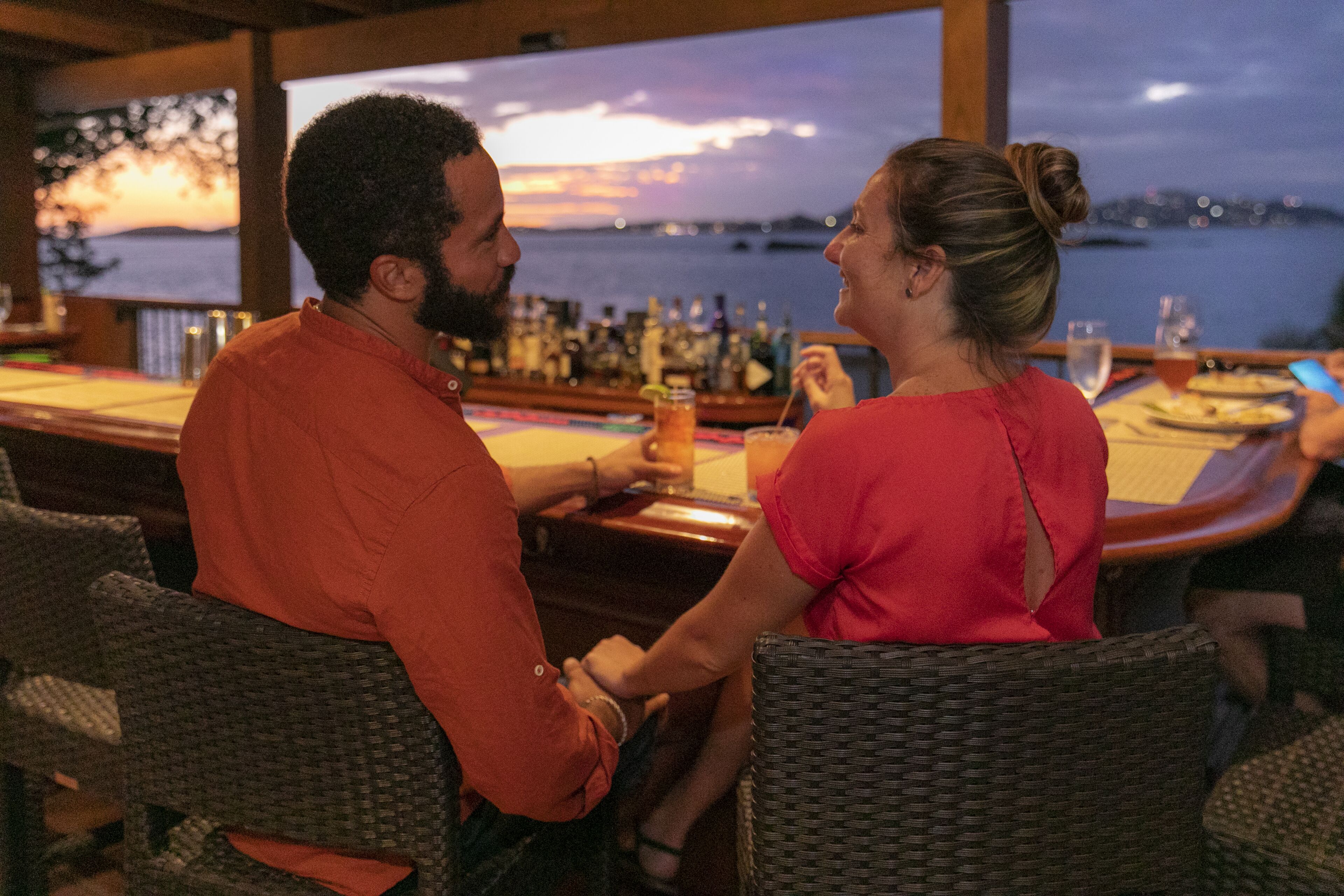 A couple seated at a bar with a view of the water and cityscape.