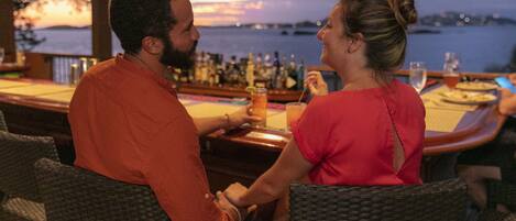 A couple seated at a bar with a view of the water and cityscape.
