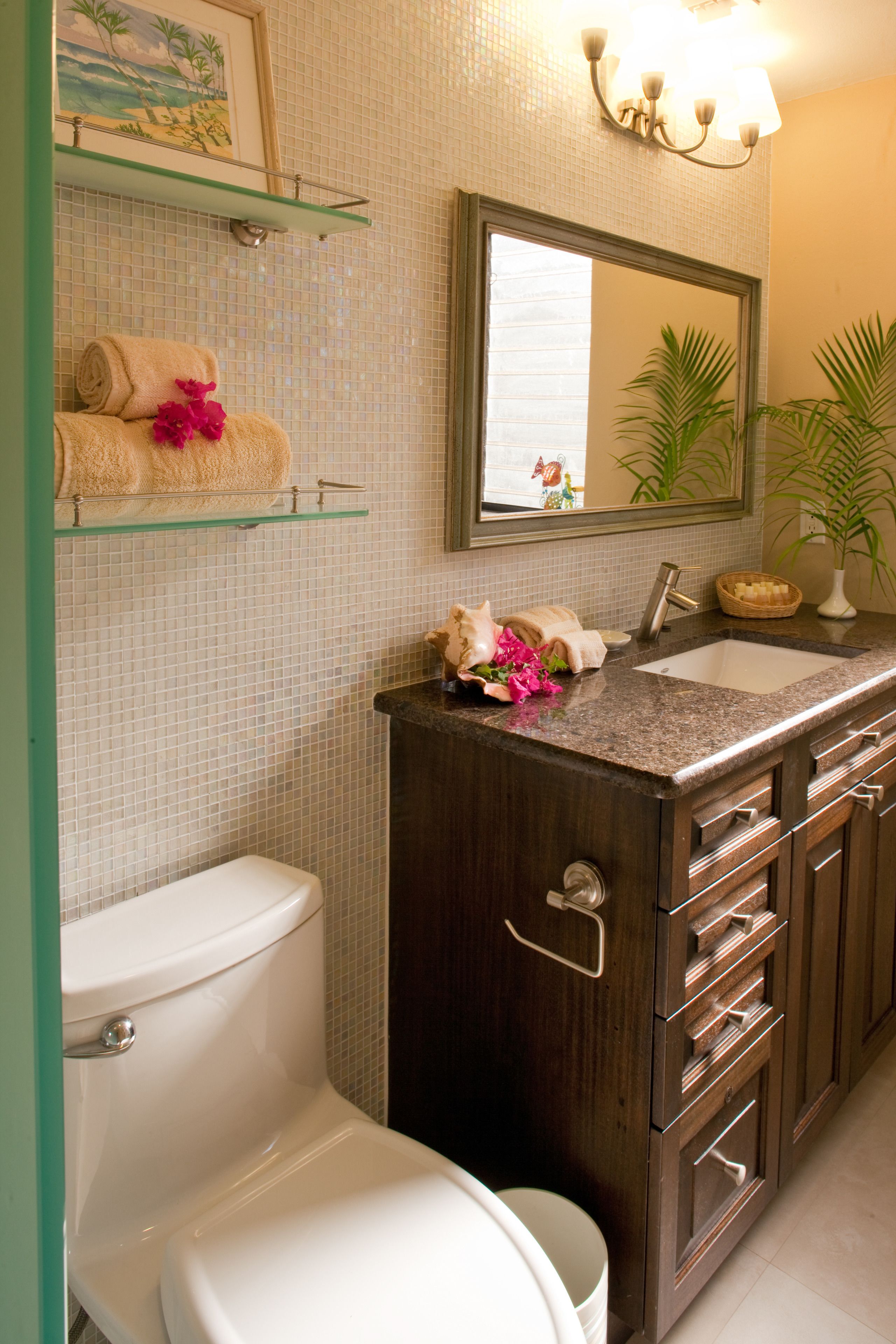 Un baño con inodoro, lavamanos, espejo y repisa con toallas y un florero.