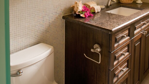 A bathroom with a toilet, a sink, a mirror, and a shelf with towels and a vase. - Gallows Point Resort (St. John)