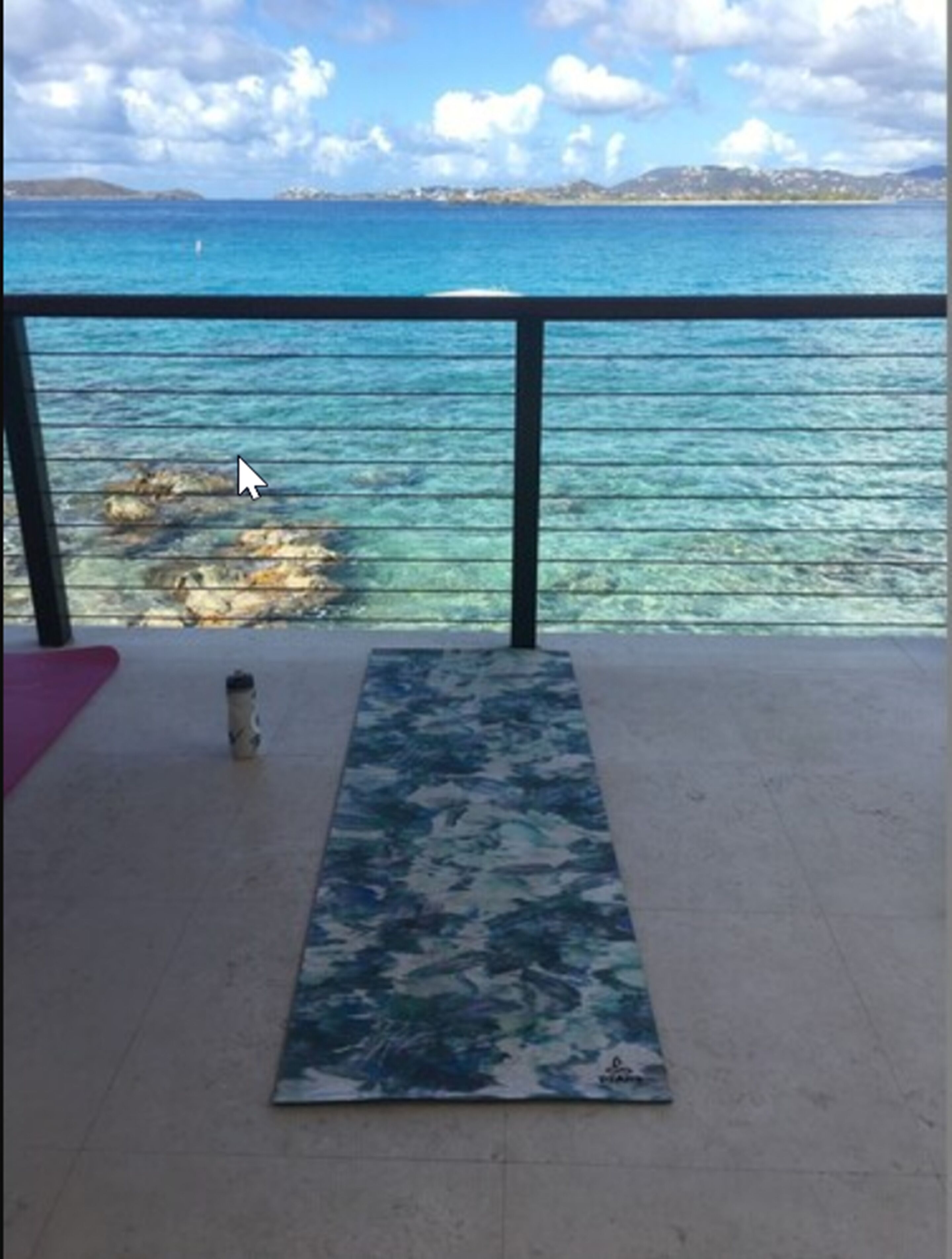A yoga mat on a balcony with a view of the sea and distant land.
