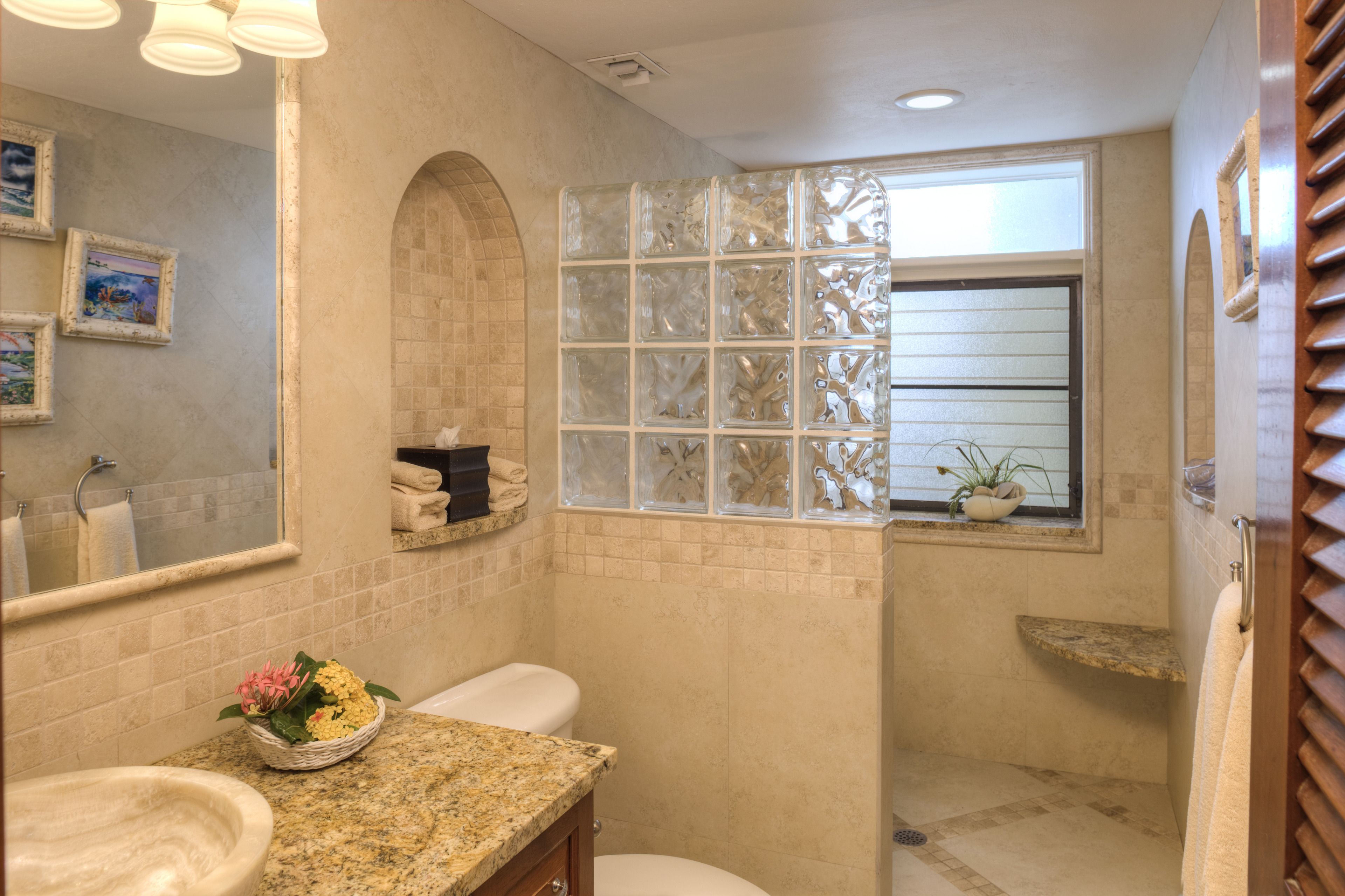 A bathroom with a granite countertop, a sink, a toilet, a shower with a glass door, and a window with a view.