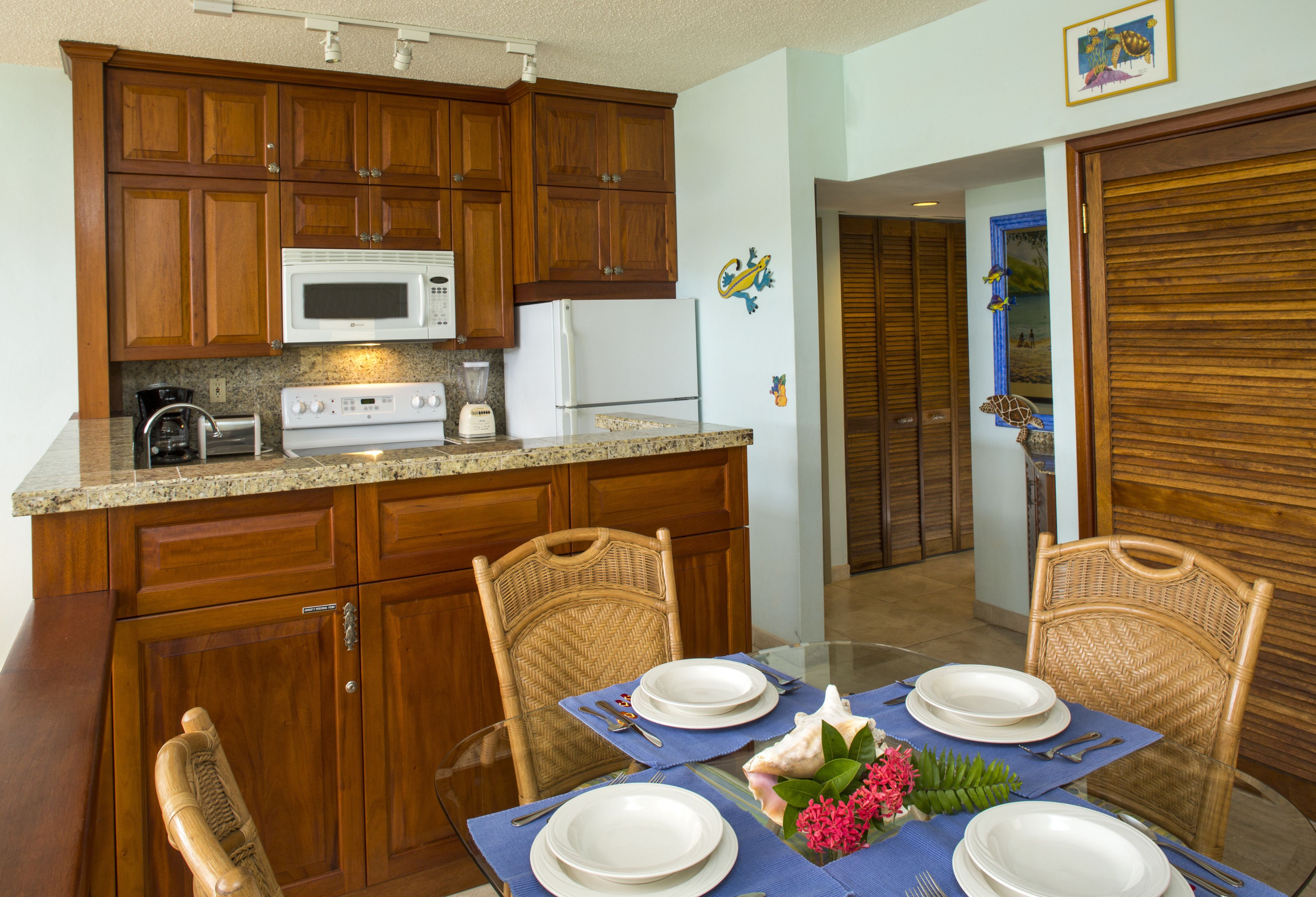 A kitchen with wooden cabinets, a microwave, and a refrigerator. There is a dining table with chairs and a blue placemat.