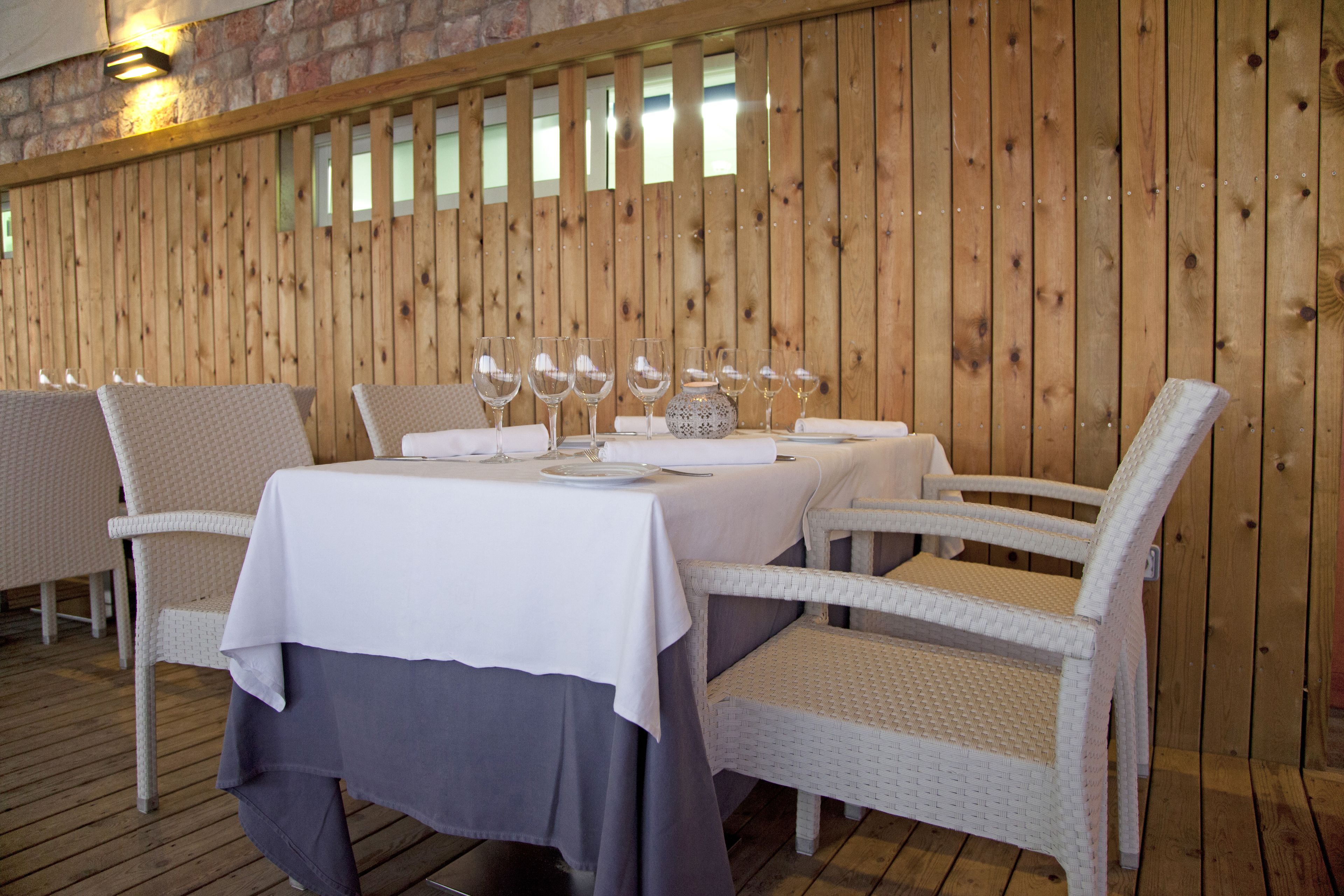 A dining area with a table set for four, surrounded by wicker chairs, against a wooden wall with vertical slats.
