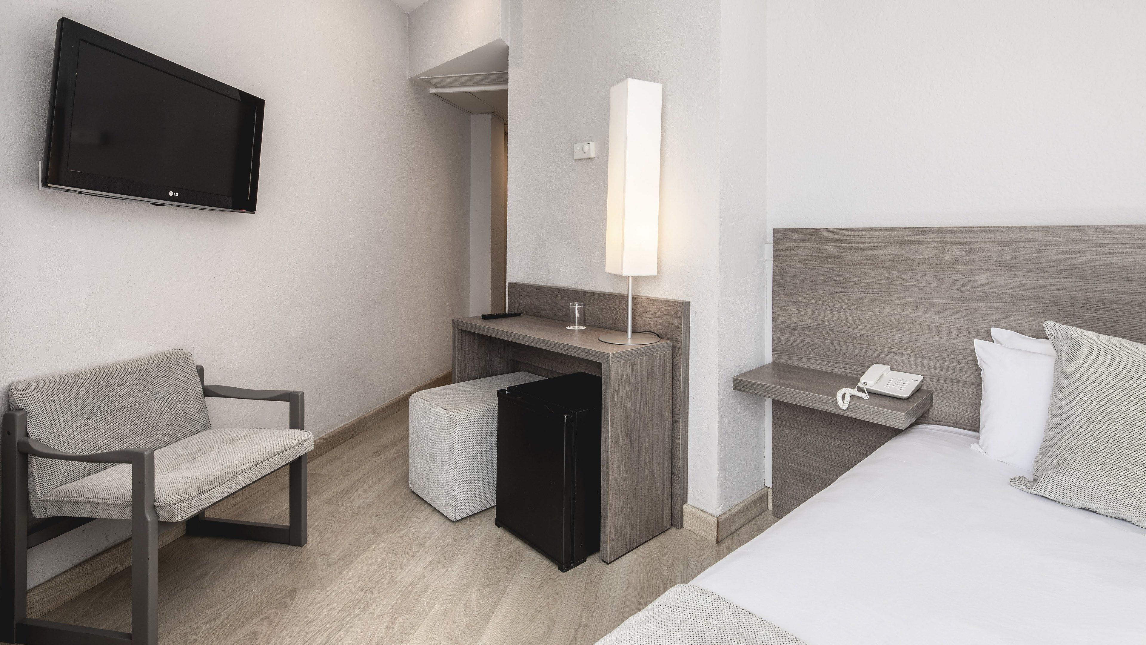 Une chambre d’hôtel avec un lit, un bureau avec une lampe, une chaise, une télévision et un téléphone.