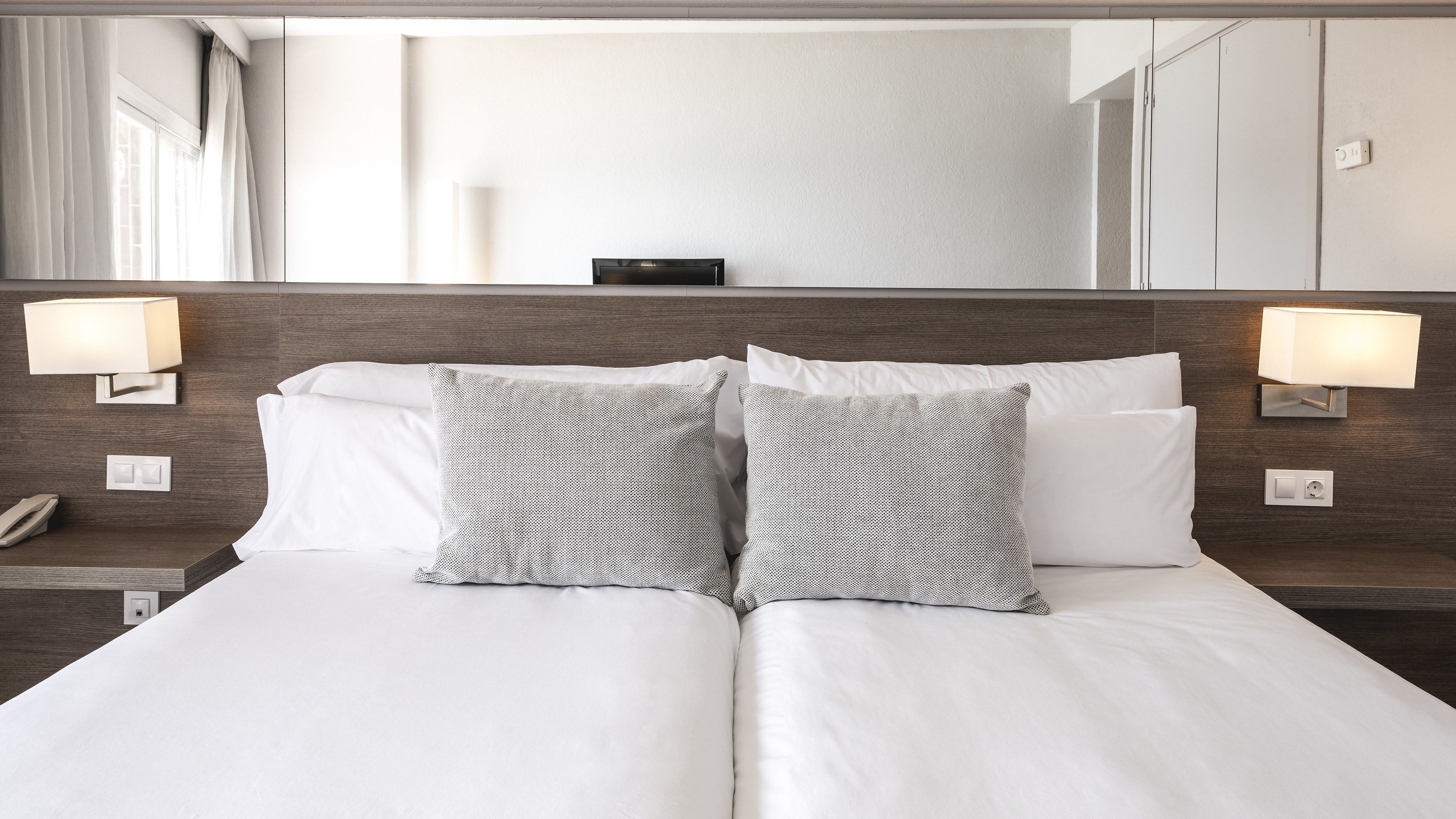 Habitación de hotel con una cama grande, dos lámparas de noche, un teléfono y un espejo en la pared.