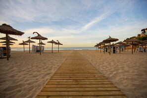 Un paseo marítimo de madera que lleva a sombrillas y sillas de playa en una arena dorada.