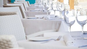 A row of white wicker chairs with white tablecloths, each set with a fork, knife, and glass. - Be Live Experience Costa Palma (Palma de Mallorca)