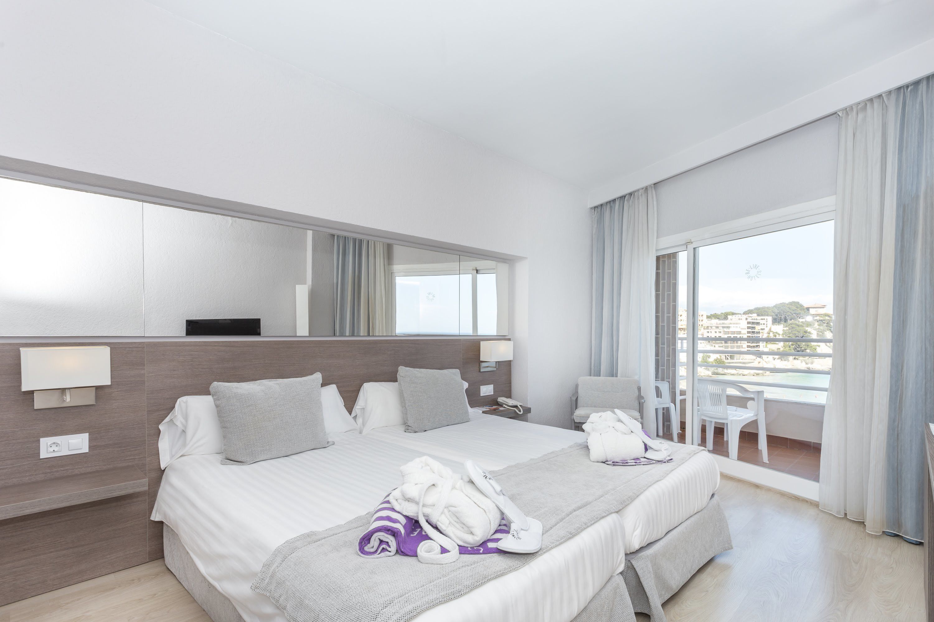 A hotel room with a large bed, a desk, a chair, and a balcony with a view.