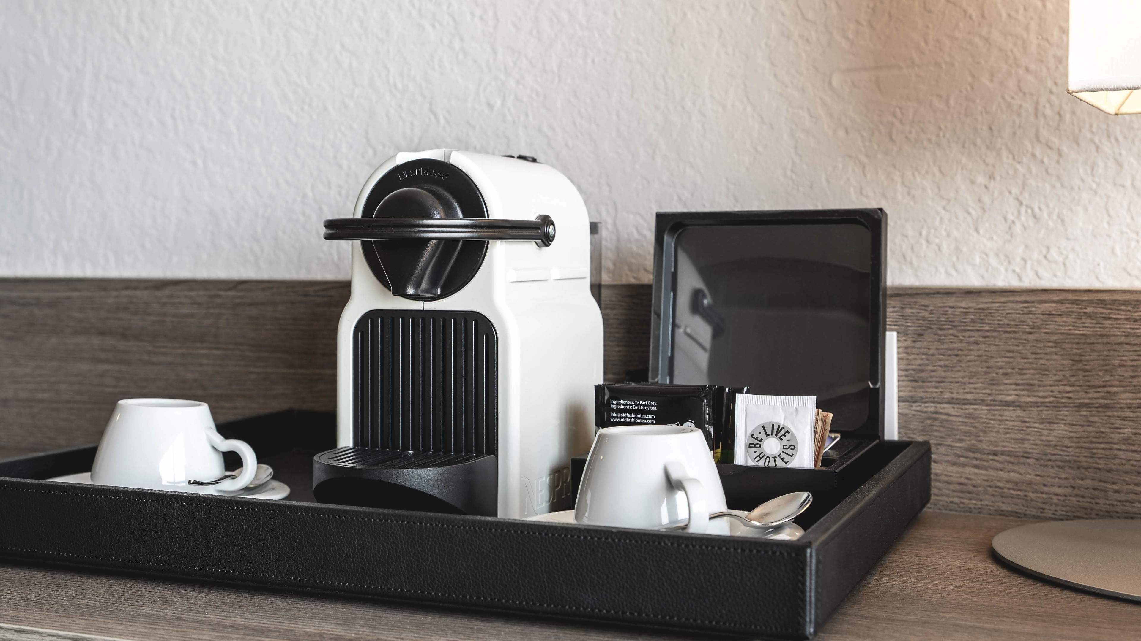 Une machine à café, un plateau avec des tasses et une cuillère, et une boîte de thé sur une surface en bois.