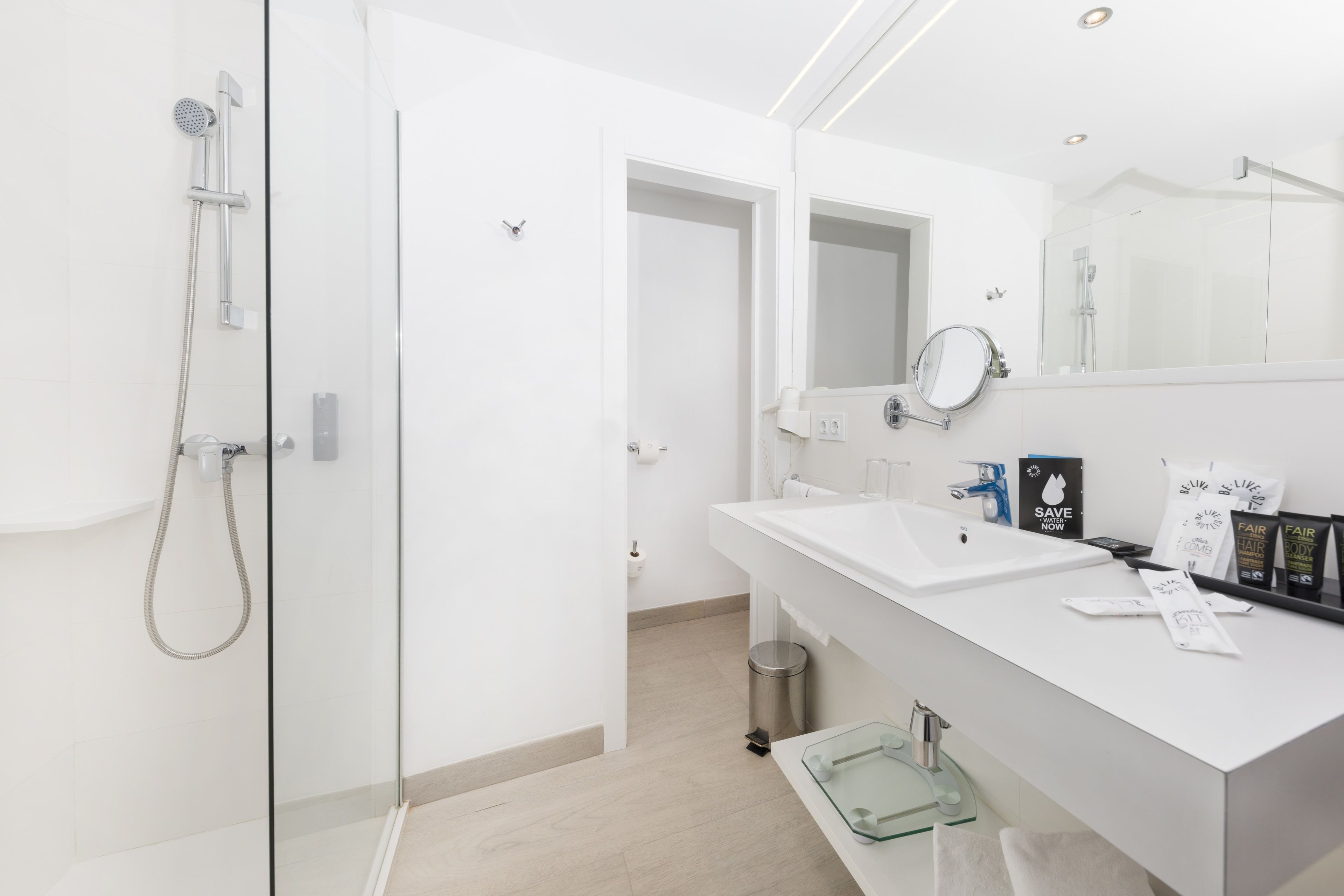Une salle de bain moderne avec une douche à l’italienne en verre, un lavabo blanc et un grand miroir.