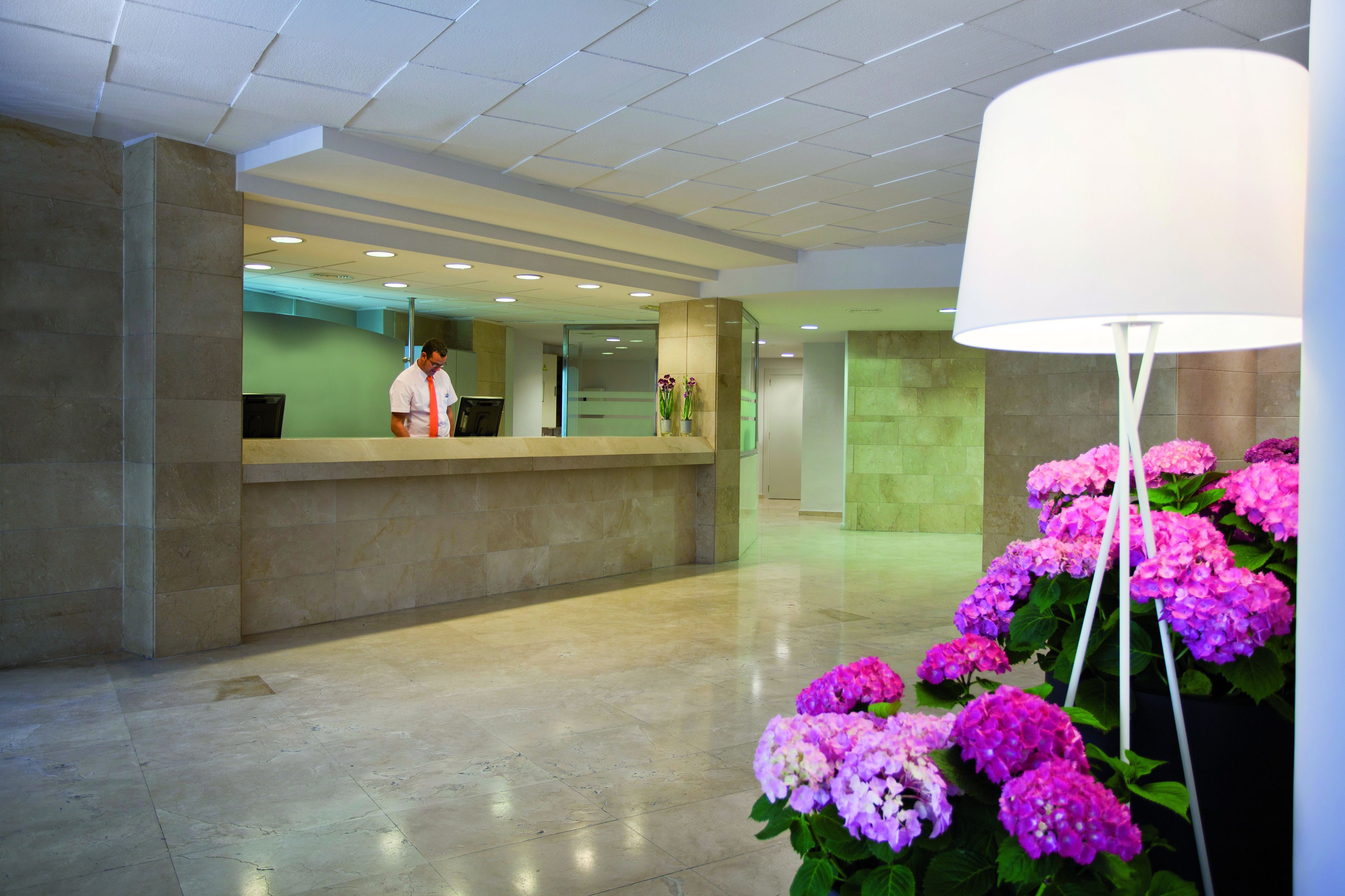 A reception area with a marble counter, a receptionist, and a large floor lamp with pink flowers.