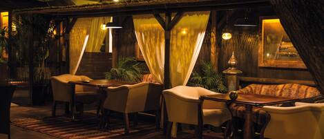 A cozy, dimly lit lounge area with a rustic wooden ceiling, cushioned seating, and a patterned rug.