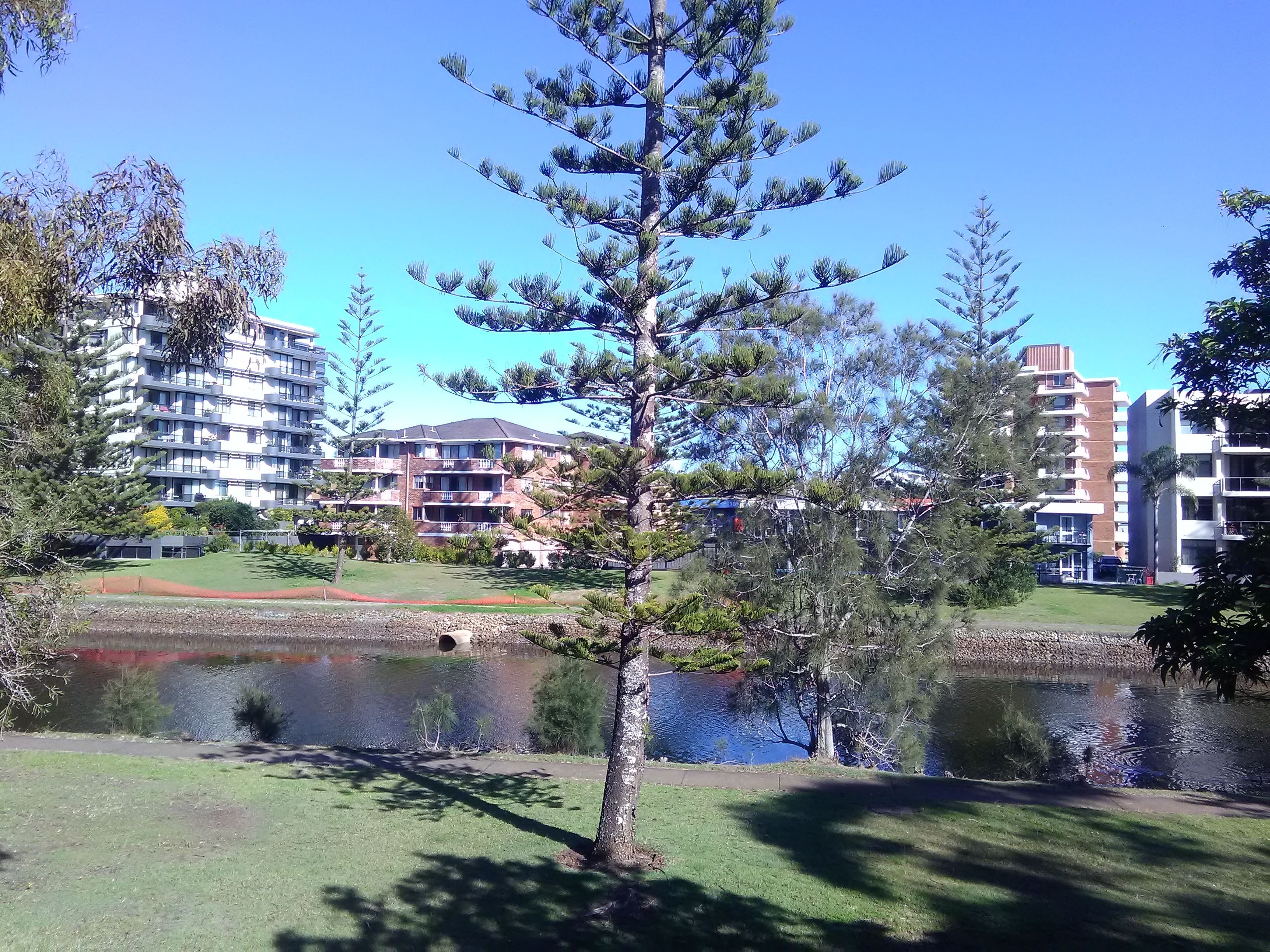 A building with multiple floors and balconies, a body of water, and surrounding greenery.