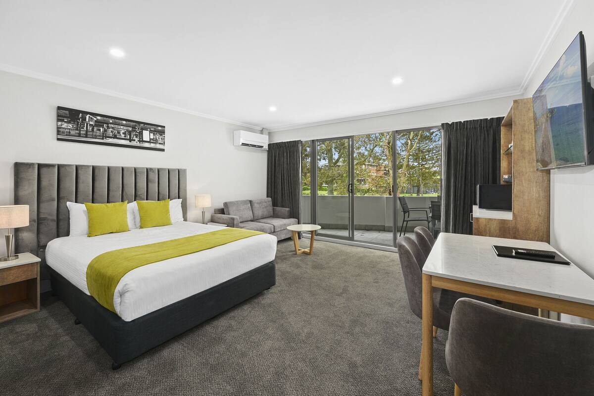 A hotel room with a large bed, a sofa, a desk, and a TV.