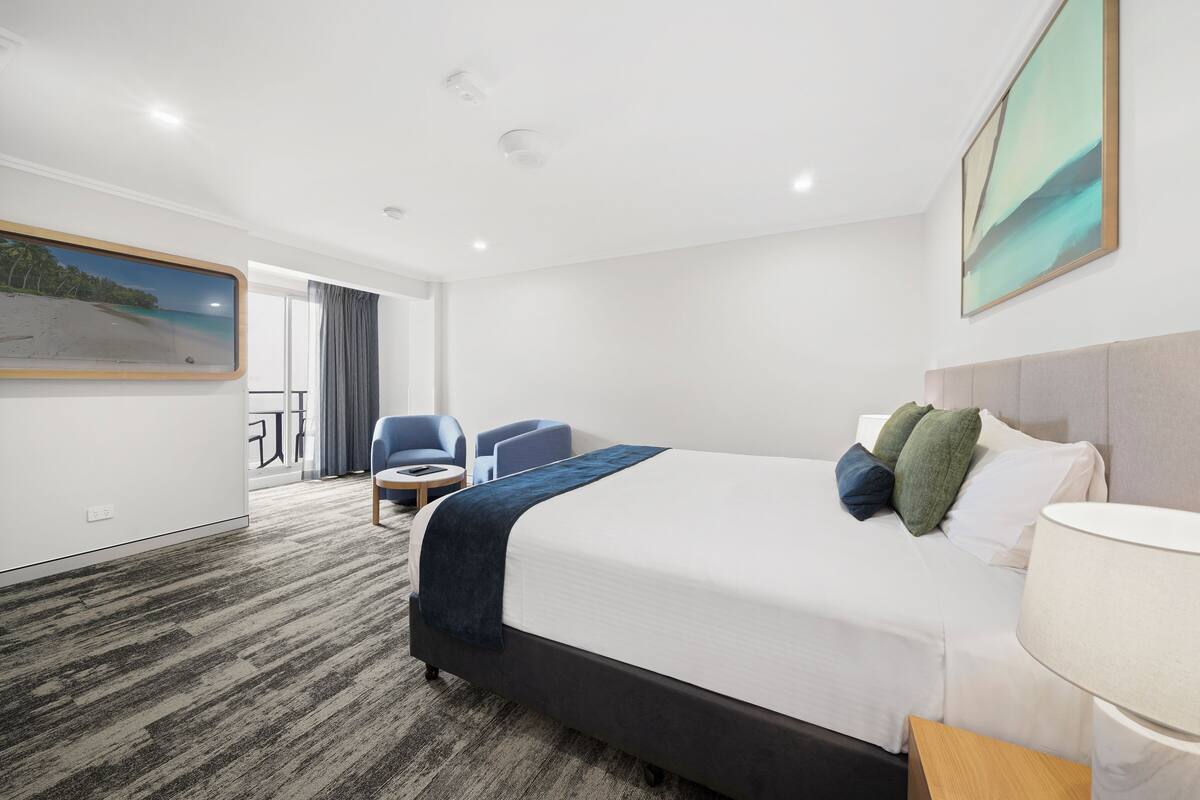 A hotel room with a bed, a desk, a chair, a window with a view, and a painting on the wall.