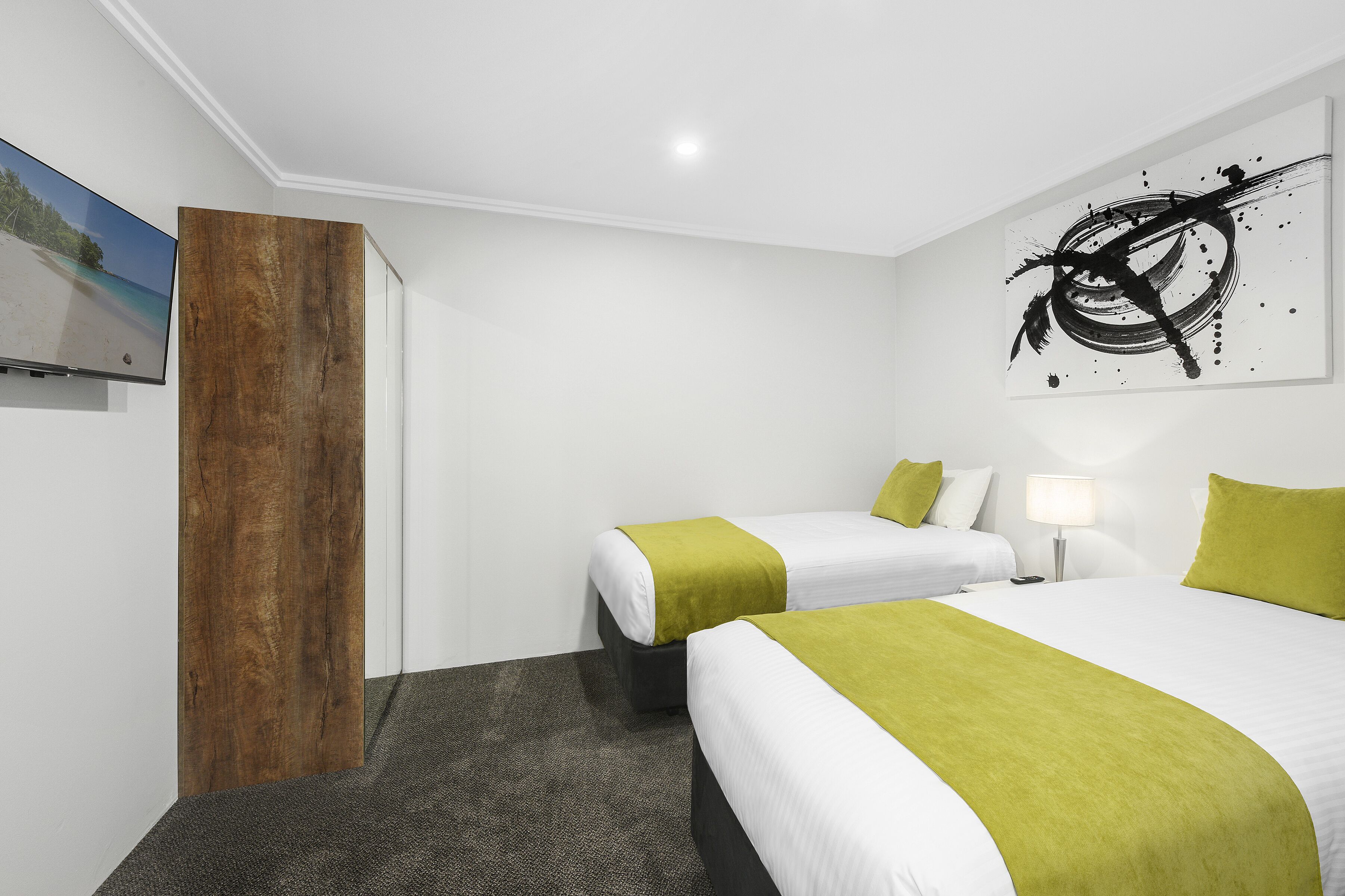 A hotel room with two beds, a wooden accent wall, a painting, and a black abstract artwork.