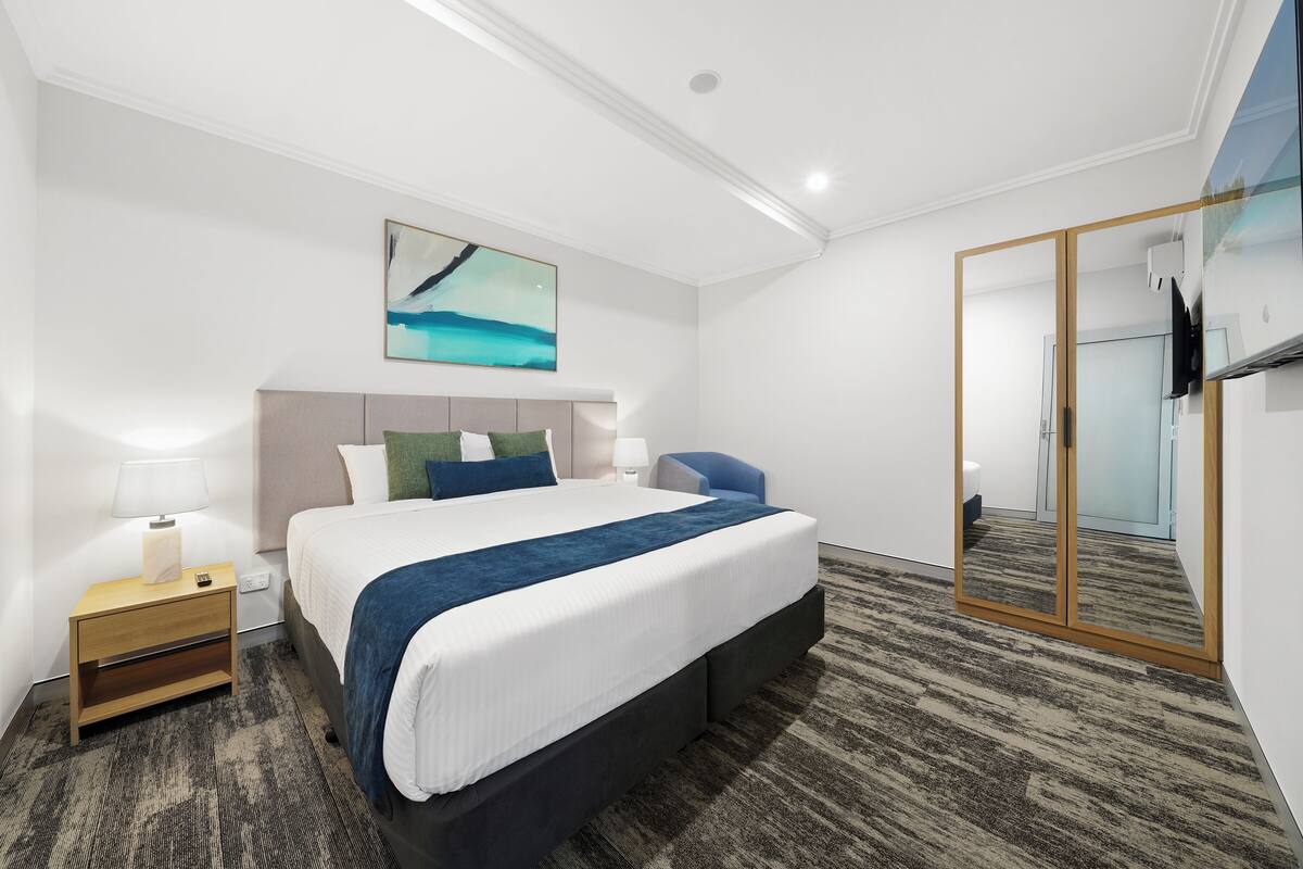A modern hotel room with a large bed, bedside tables, a mirror, and a painting on the wall.