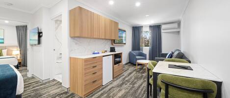 A modern hotel room with a kitchenette, a dining area, a bed, and a TV.