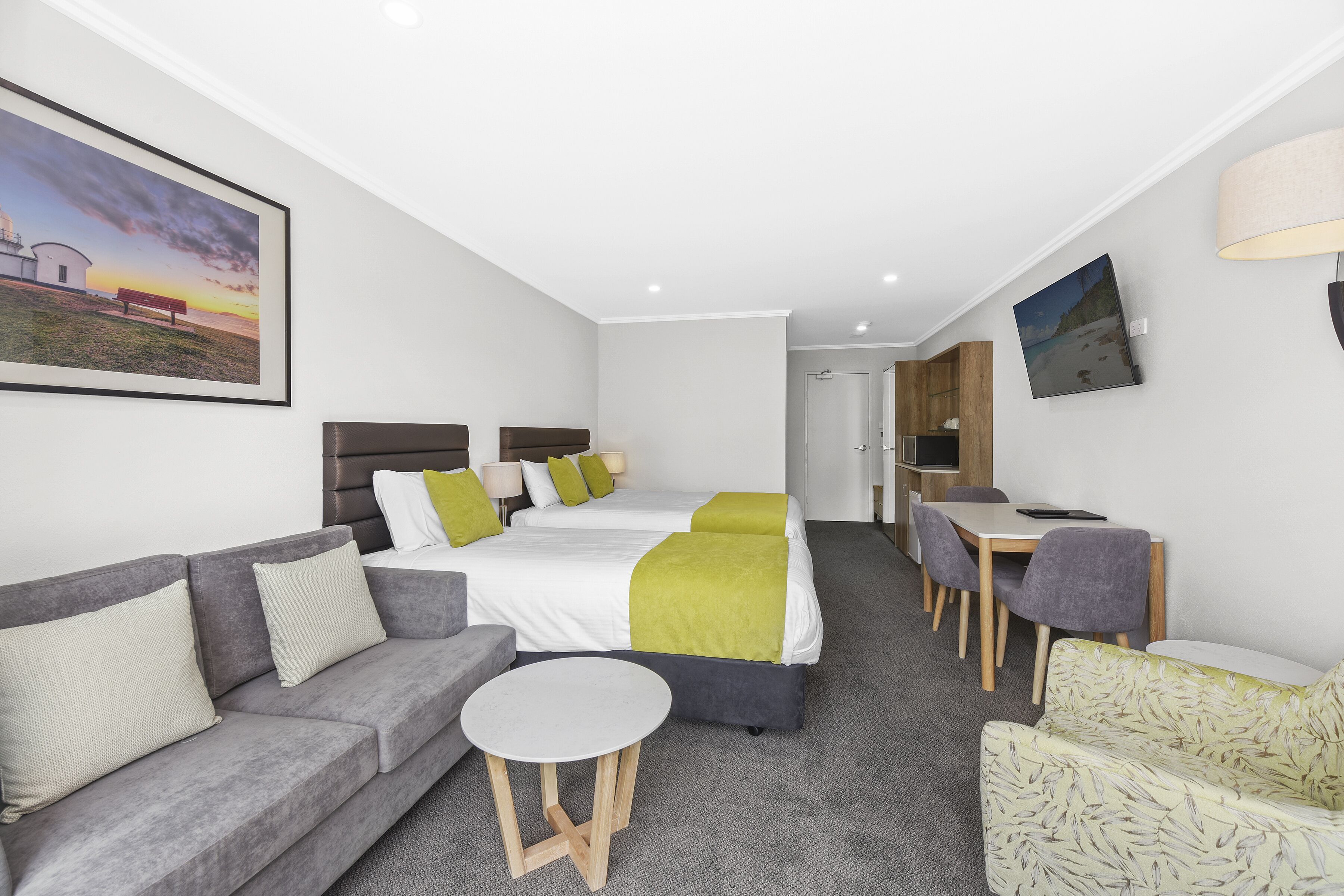 Habitació d'hotel moderna amb llit, sofà, taula de menjador i televisió.