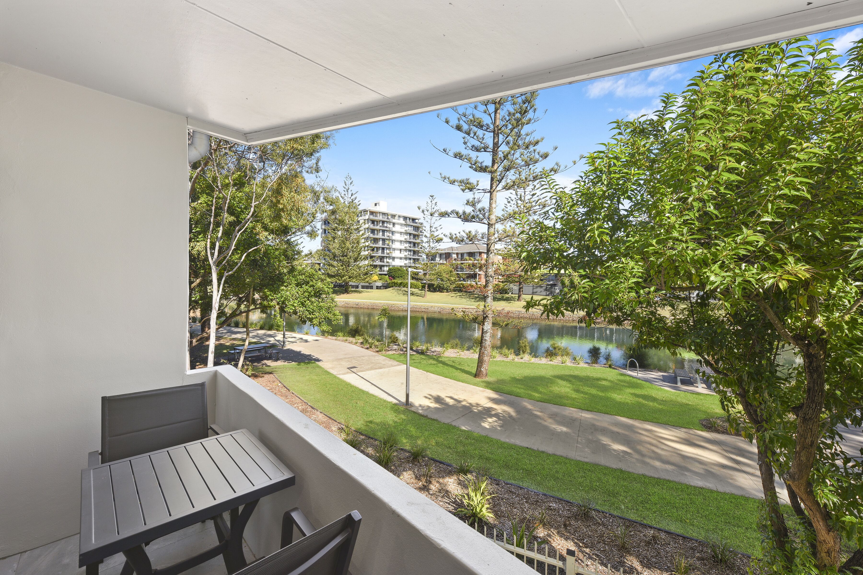 A balcony with a view of a landscaped area, including a pond and buildings in the background.
