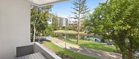 A balcony with a view of a landscaped area, including a pond and buildings in the background.