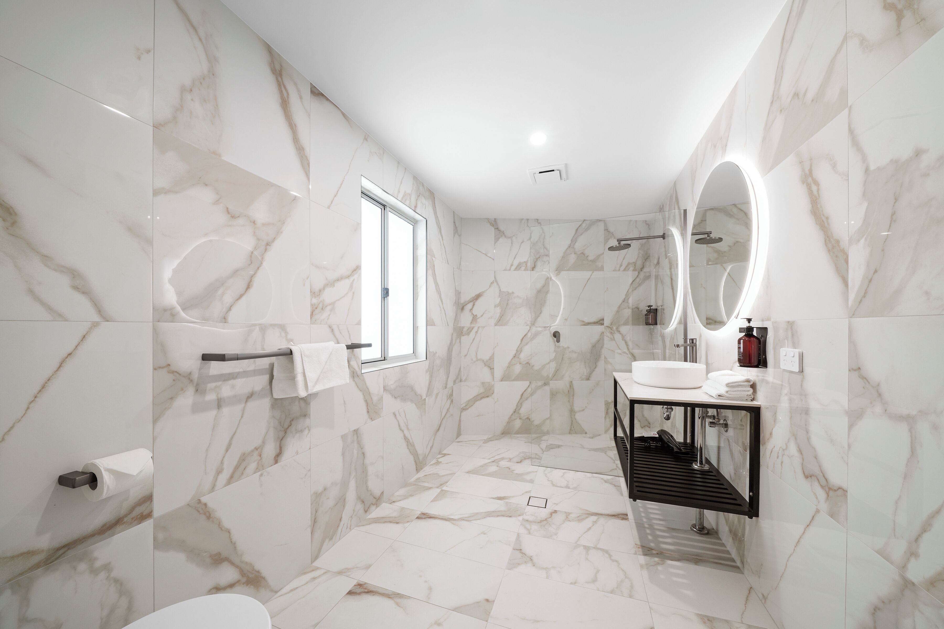 Un baño moderno con paredes de mármol, un espejo grande, un lavabo y una ducha.
