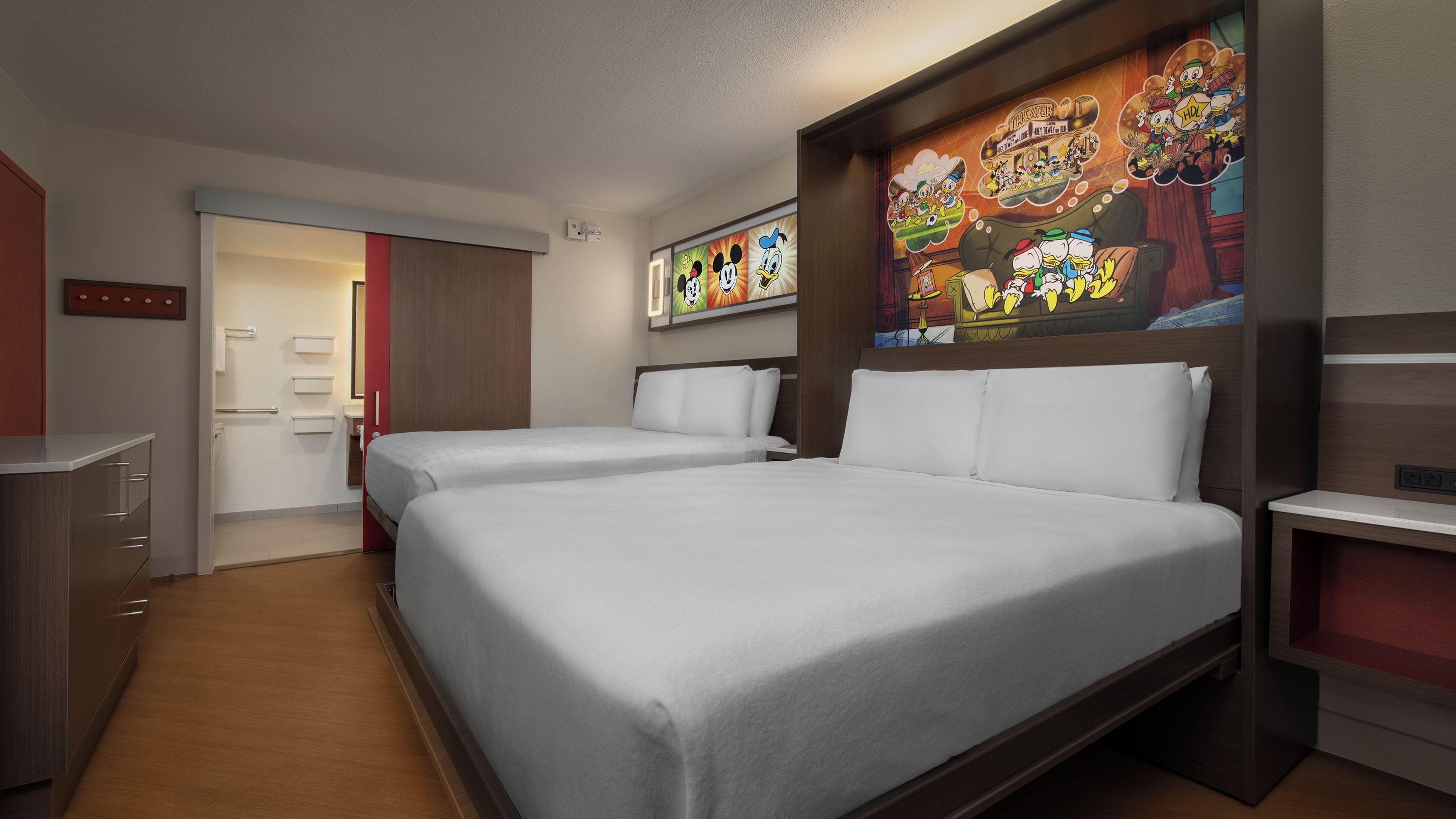 A hotel room with two beds, a desk, a dresser, and a large wall mural.