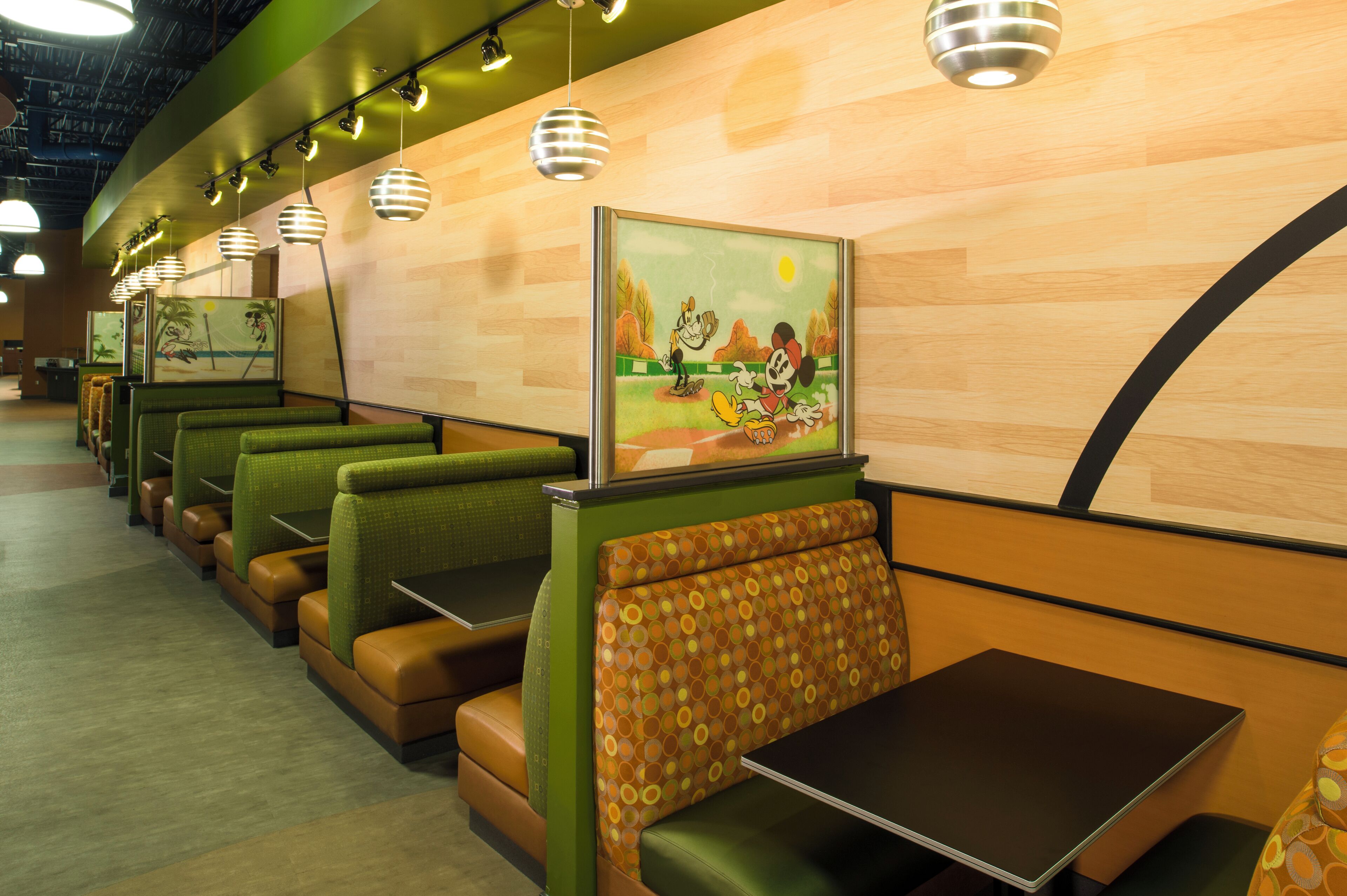 A restaurant with booths and tables, featuring a baseball-themed mural and hanging pendant lights.