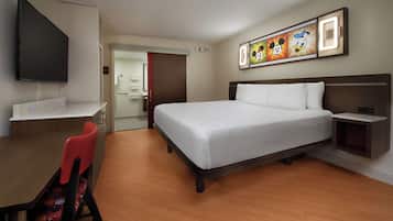 A hotel room with a bed, a desk, a chair, and a TV mounted on the wall.