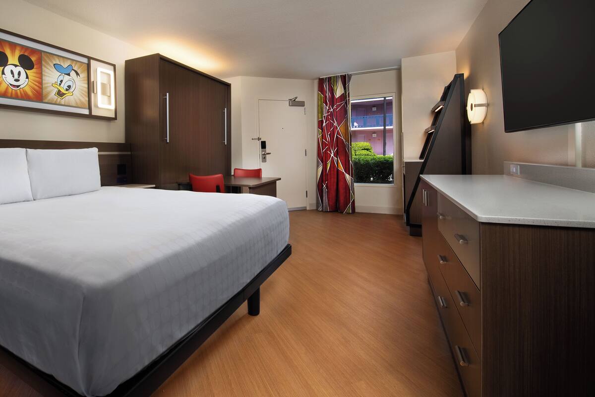 A hotel room with a large bed, a desk, a chair, a dresser, and a TV.