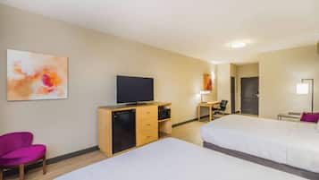 Ein Hotelzimmer mit zwei Betten, einem Schreibtisch, einem Fernseher und einem Sessel.