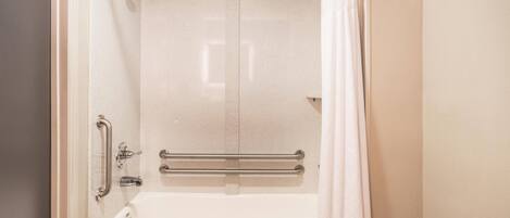 A bathroom with a bathtub, grab bars, and a shower curtain.