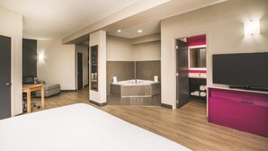 Una habitación de hotel moderna con una cama grande, un televisor, un baño con bañera y un armario rosa.