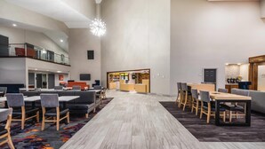 Un amplio vestíbulo de hotel con techo alto, una recepción central, varias áreas de descanso y un entrepiso con barandilla.