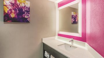 Un bagno con un lavandino bianco, uno specchio con cornice rosa e un quadro astratto appeso alla parete.