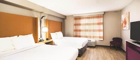 Habitación de hotel con dos camas, un escritorio con lámpara, una silla, televisión y ventana con cortinas a rayas.