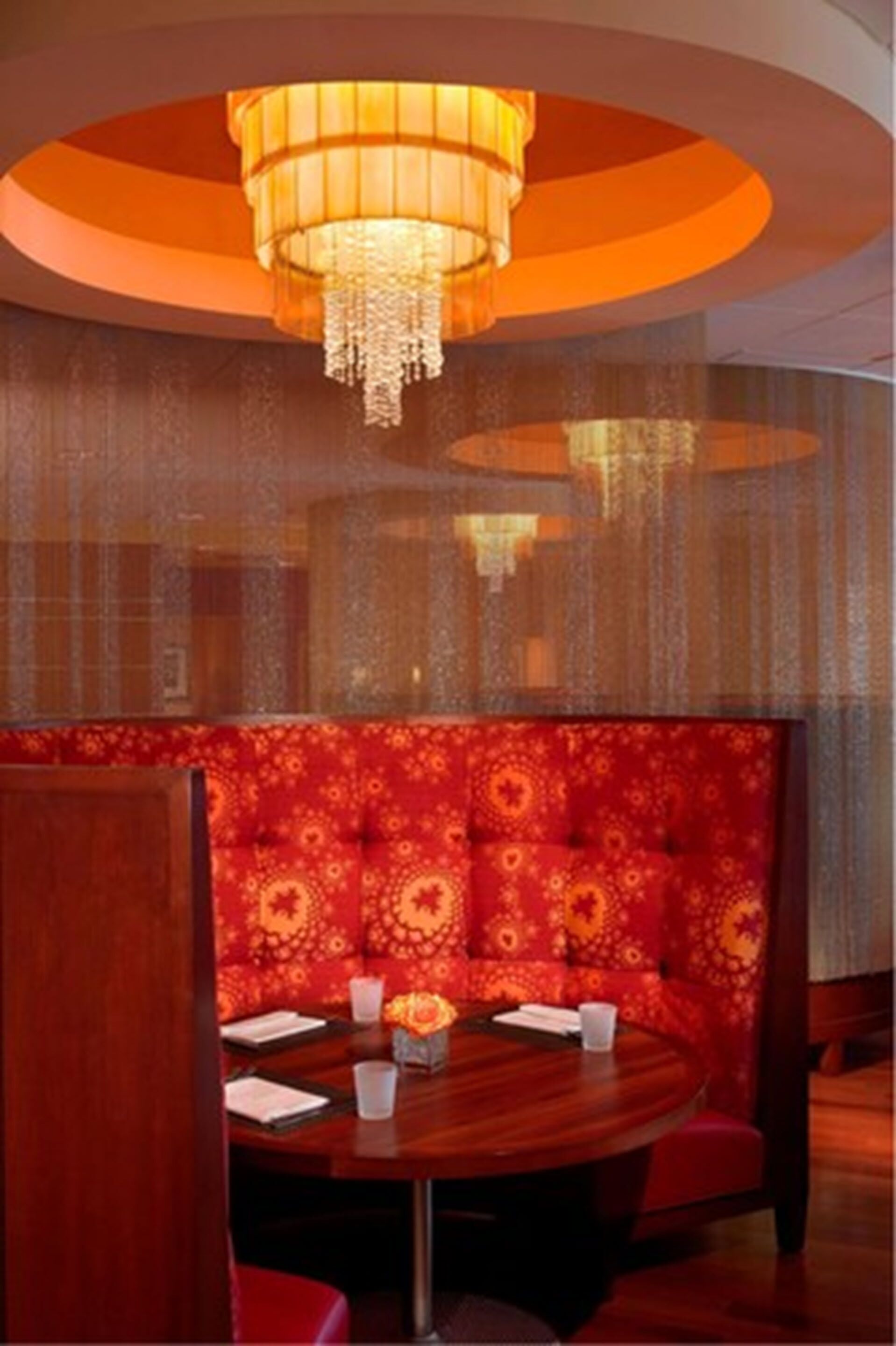 Une table ronde avec des banquettes rouges, un lustre et un mur orné de motifs.