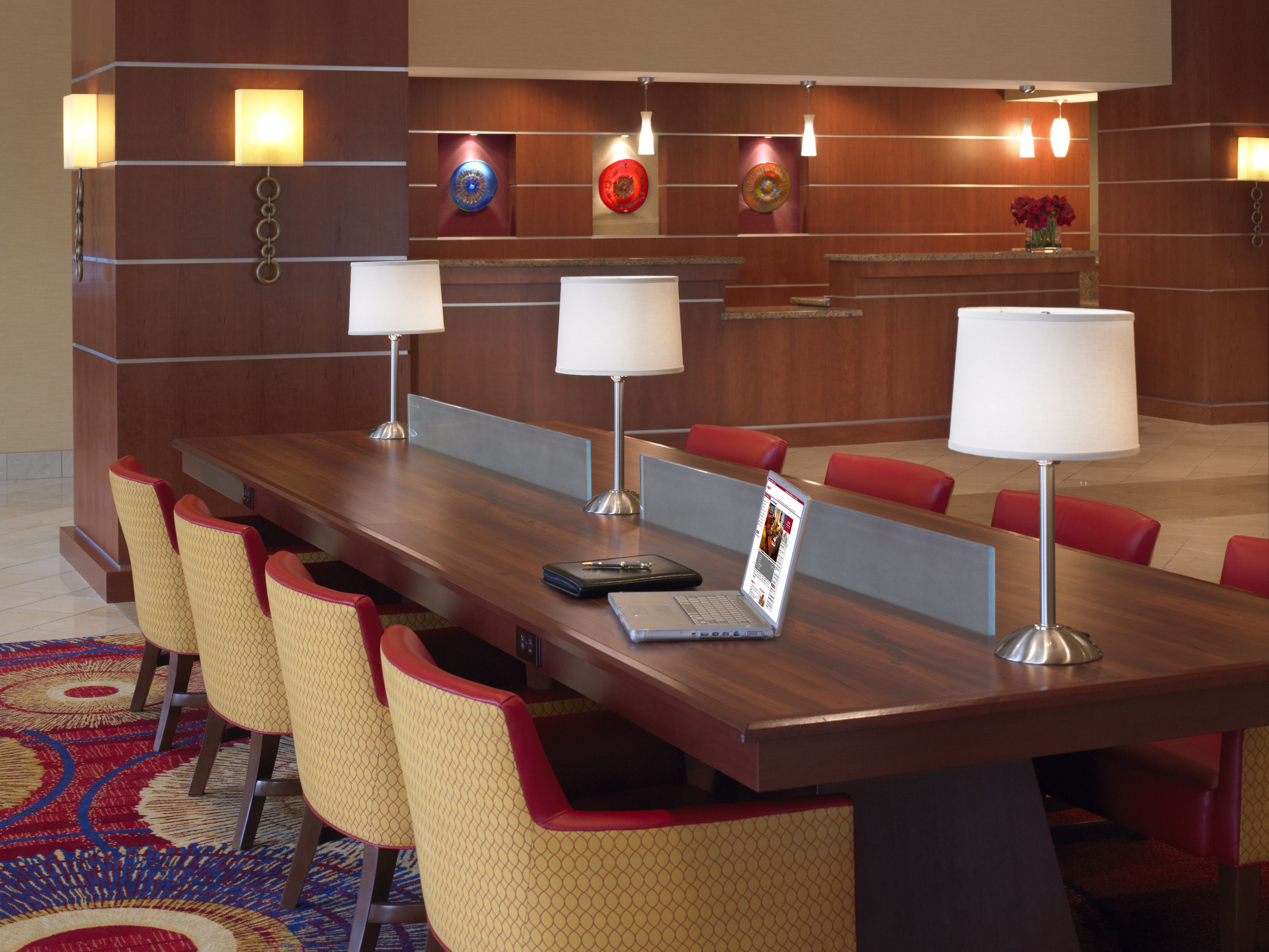 A conference room with a long table, red and yellow chairs, and two lamps.
