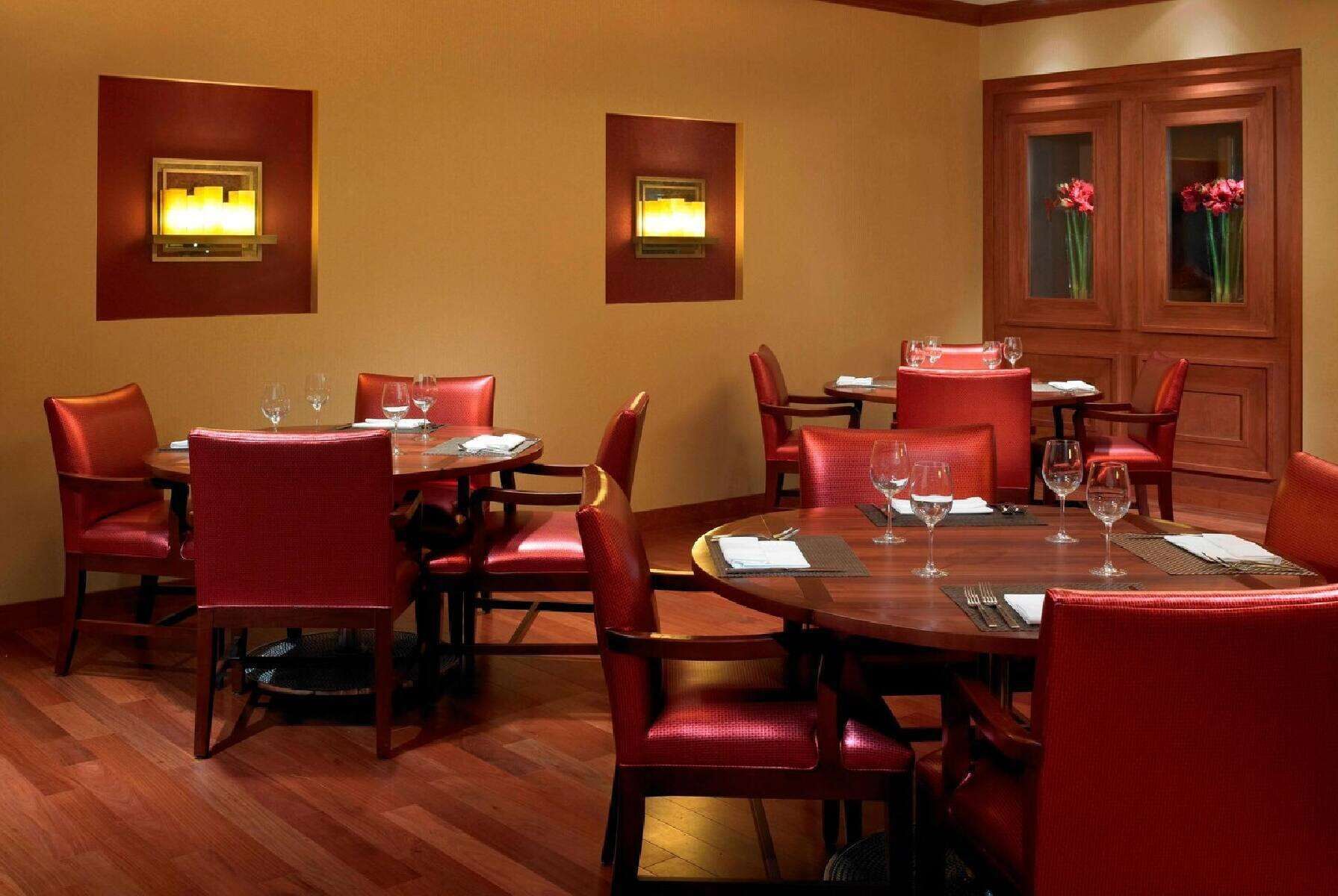 A dining area with round tables, red upholstered chairs, and wall-mounted light fixtures.